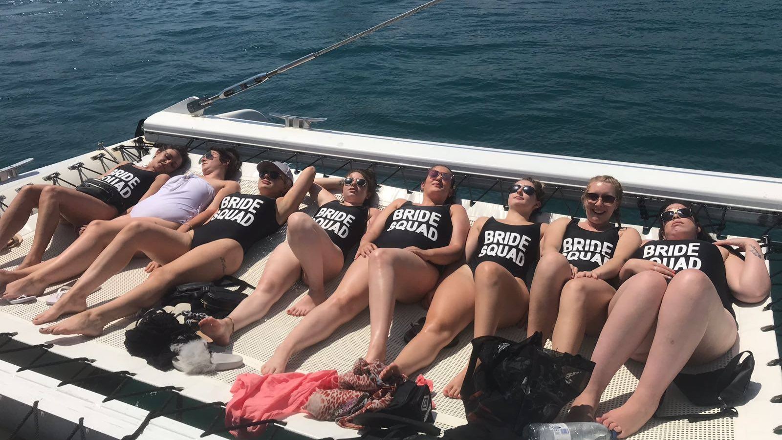 women sunbathing on a boat, wearing Bride Squad bathing suits
